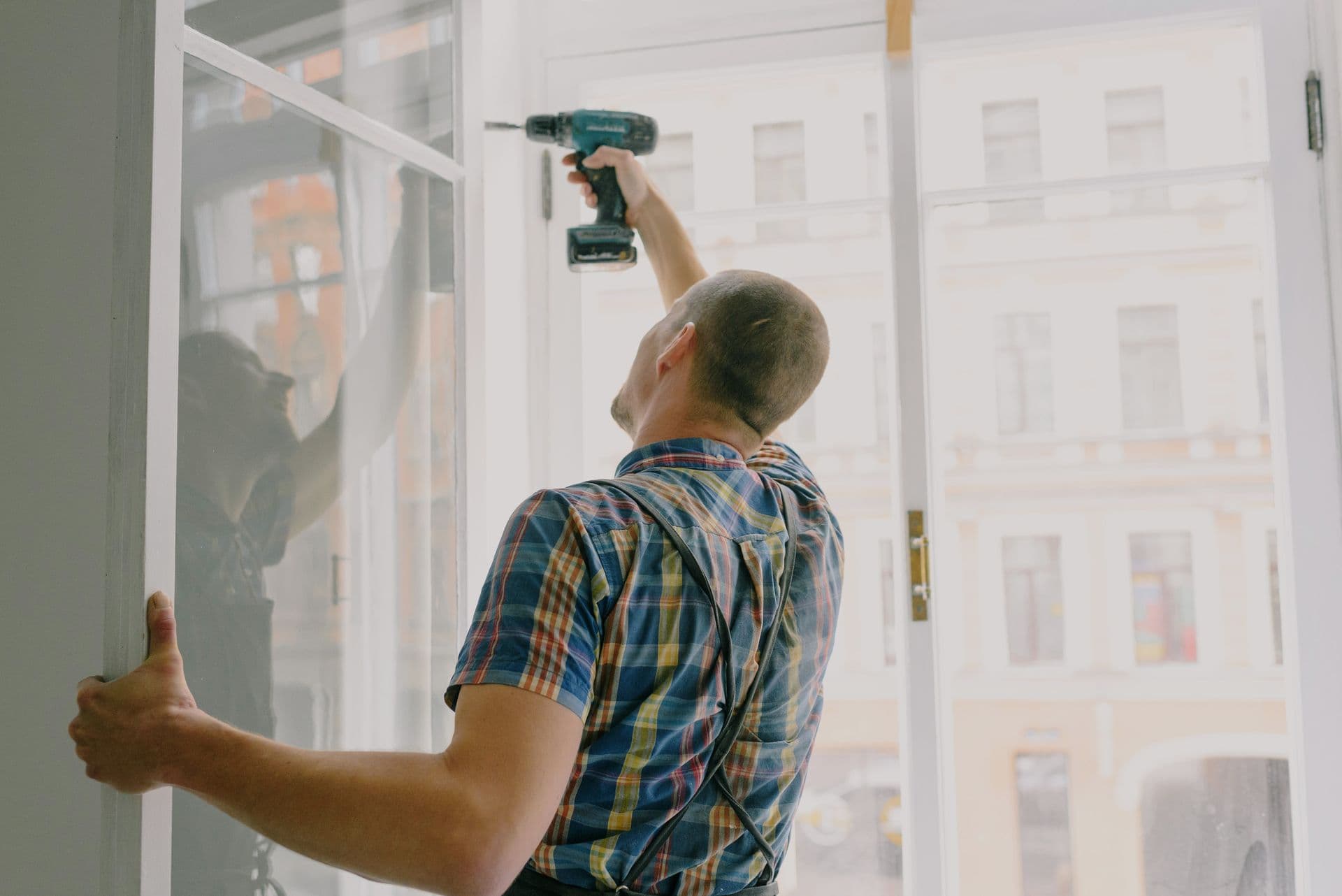 Tradesman fitting a window frame with a cordless drill